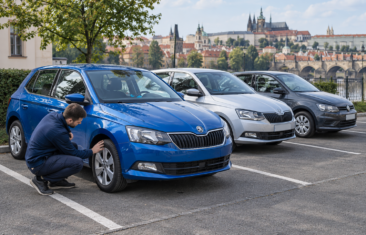 Zaměstnanec kontroluje volant modrého auta na parkovišti vedle dvou dalších aut.